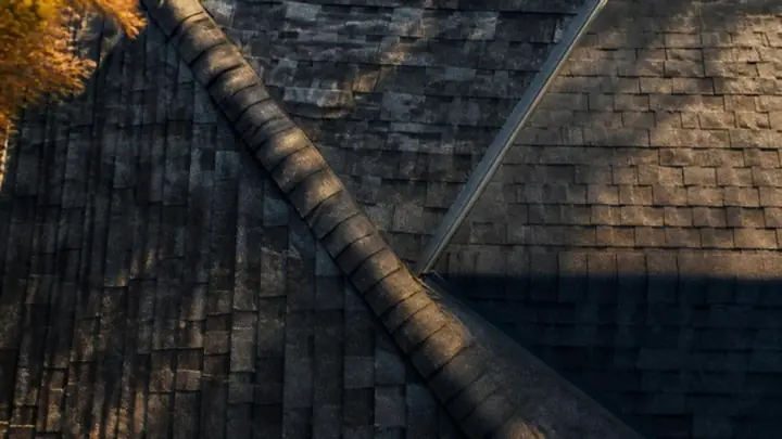 Overhead view of new dark architectural shingle courses meeting at a ridge and a valley in low evening sun
